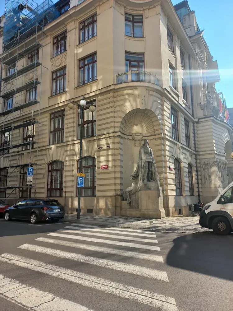 Estatua de un caballero con capa en la esquina de un edificio clásico, con un paso de peatones en primer plano.