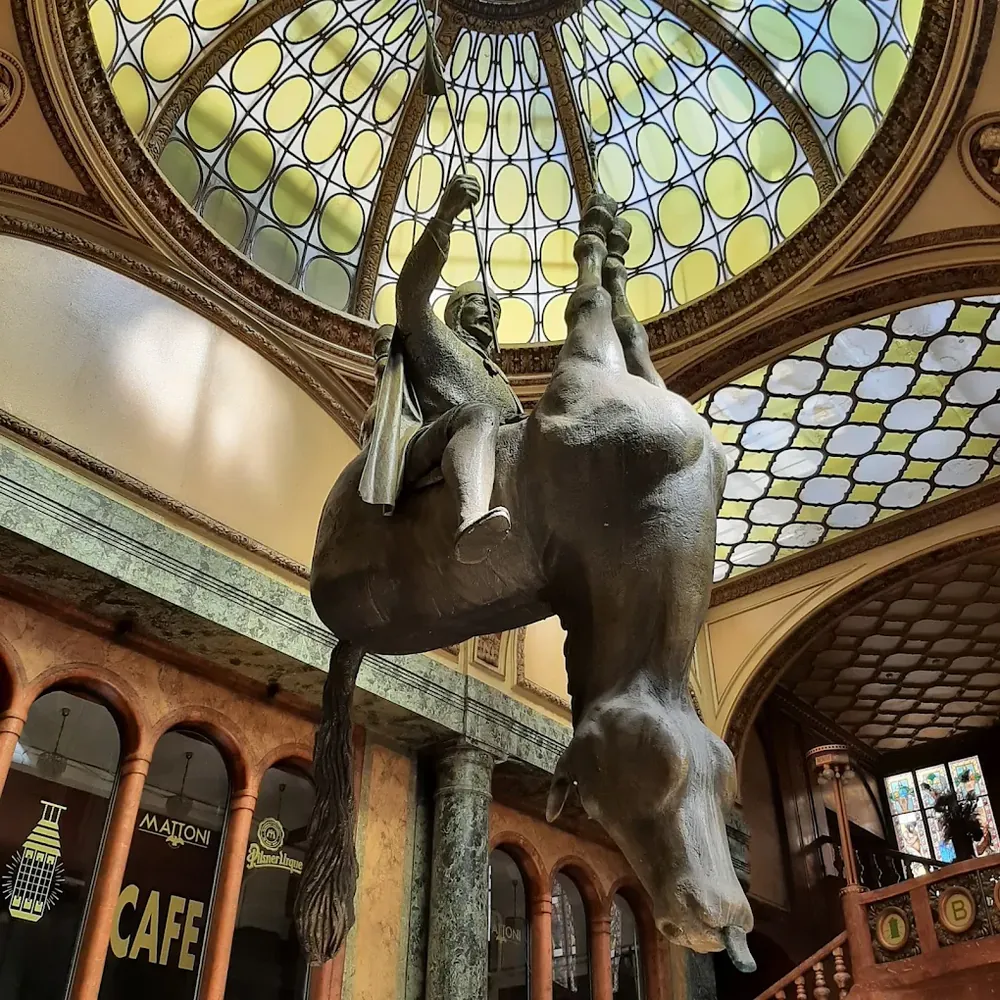Escultura colgante de San Wenceslao montado en un caballo boca abajo bajo una cúpula de vitrales de colores.