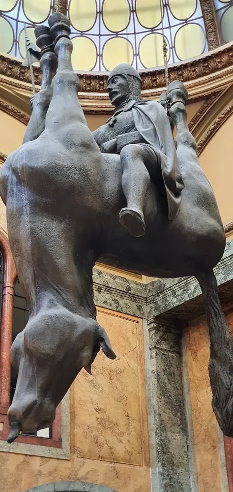 Estatua colgante de un caballero montado en un caballo muerto que cuelga boca abajo desde el techo abovedado.