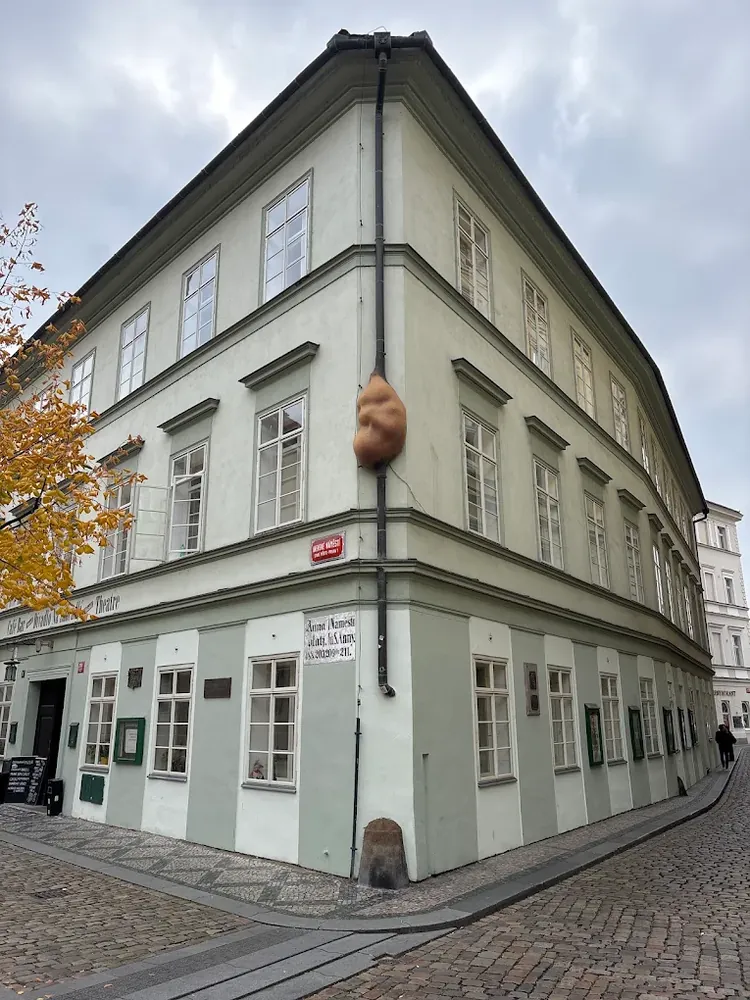 Escultura marrón con forma de embrión humano en la esquina de un edificio claro con bajante pluvial.