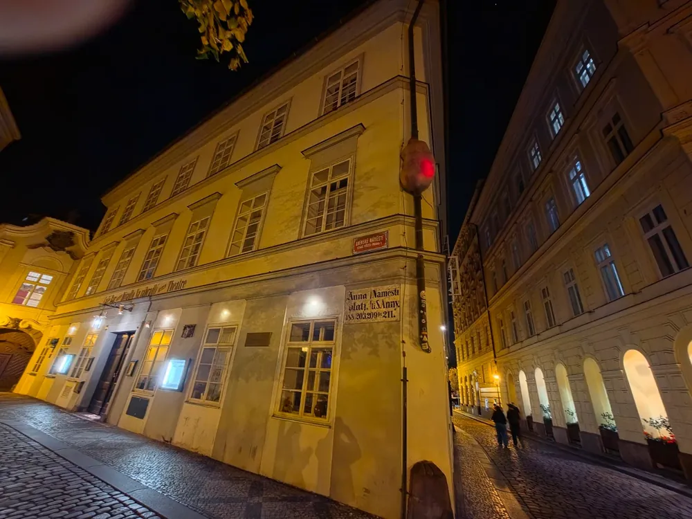 Vista nocturna de un edificio antiguo con una escultura iluminada en su esquina, en una calle empedrada.