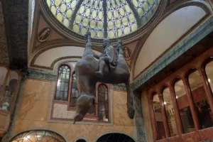 Escultura colgante de un caballo invertido con un jinete en su lomo, bajo una cúpula de vidrio en un palacio de estilo his...