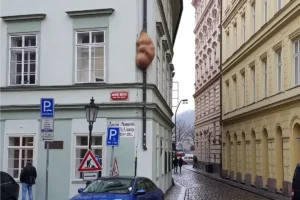 Escultura marrón con forma de embrión humano en la esquina de un edificio claro en Praga.