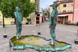 Dos estatuas de hombres metálicos y segmentados orinando en una fuente con forma de la República Checa.