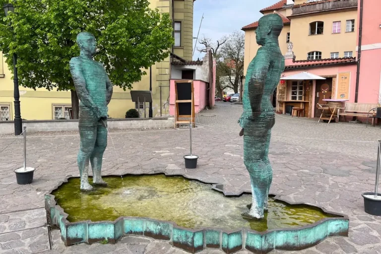 Dos estatuas de hombres metálicos y segmentados orinando en una fuente con forma de la República Checa.