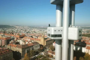 Vista panorámica de la Torre Žižkov en Praga, mostrando sus columnas metálicas y la plataforma con una escultura.