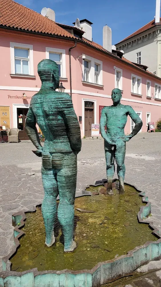 Dos estatuas de bronce verde con forma de hombre en una fuente con la silueta de la República Checa.