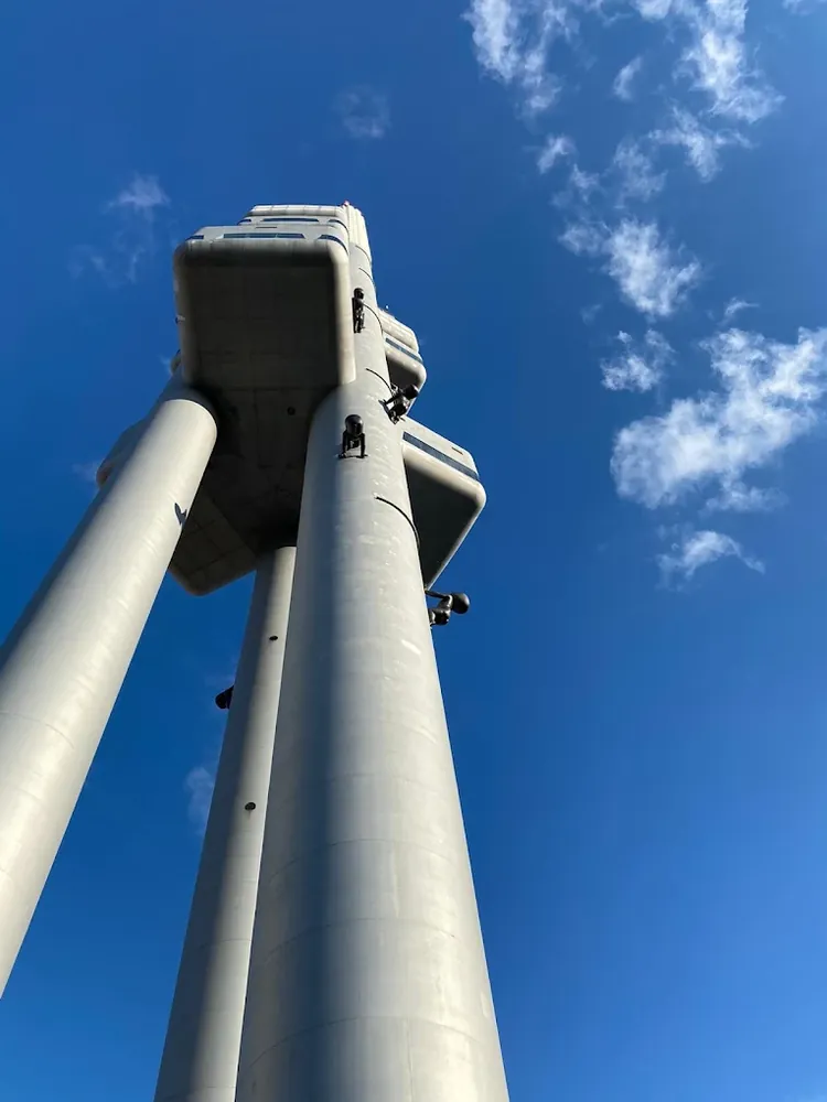 Vista en contrapicado de la Torre Žižkov con sus pilares grises contra un cielo azul con nubes dispersas.