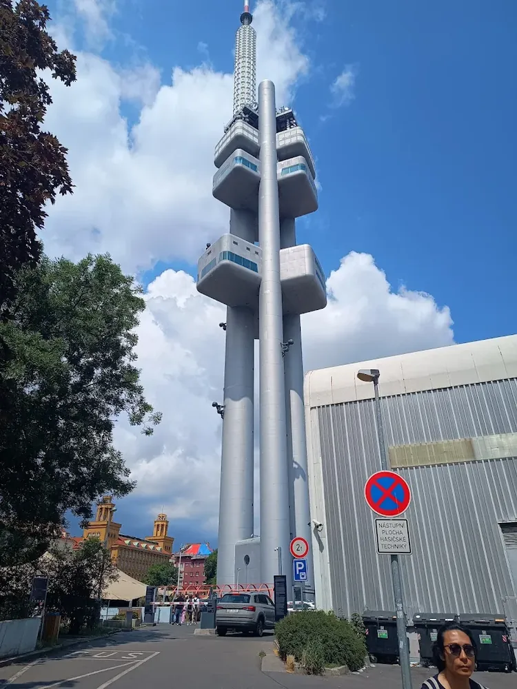 La torre Žižkov destaca con sus tres pilares grises y cápsulas de observación bajo un cielo azul con nubes.