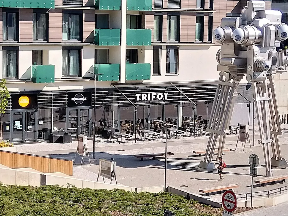 Fachada de TRIFOT con terraza y una gran escultura metálica de una cámara de cine con múltiples ojos.