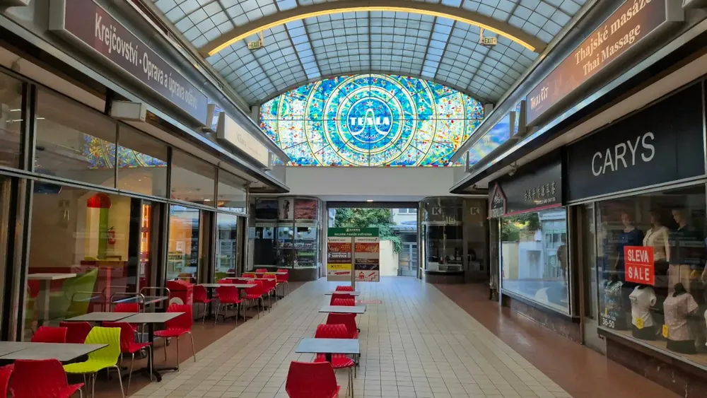 Galería comercial cubierta con un gran vitral colorido al fondo que dice "Tesla" bajo un techo abovedado de cristal.